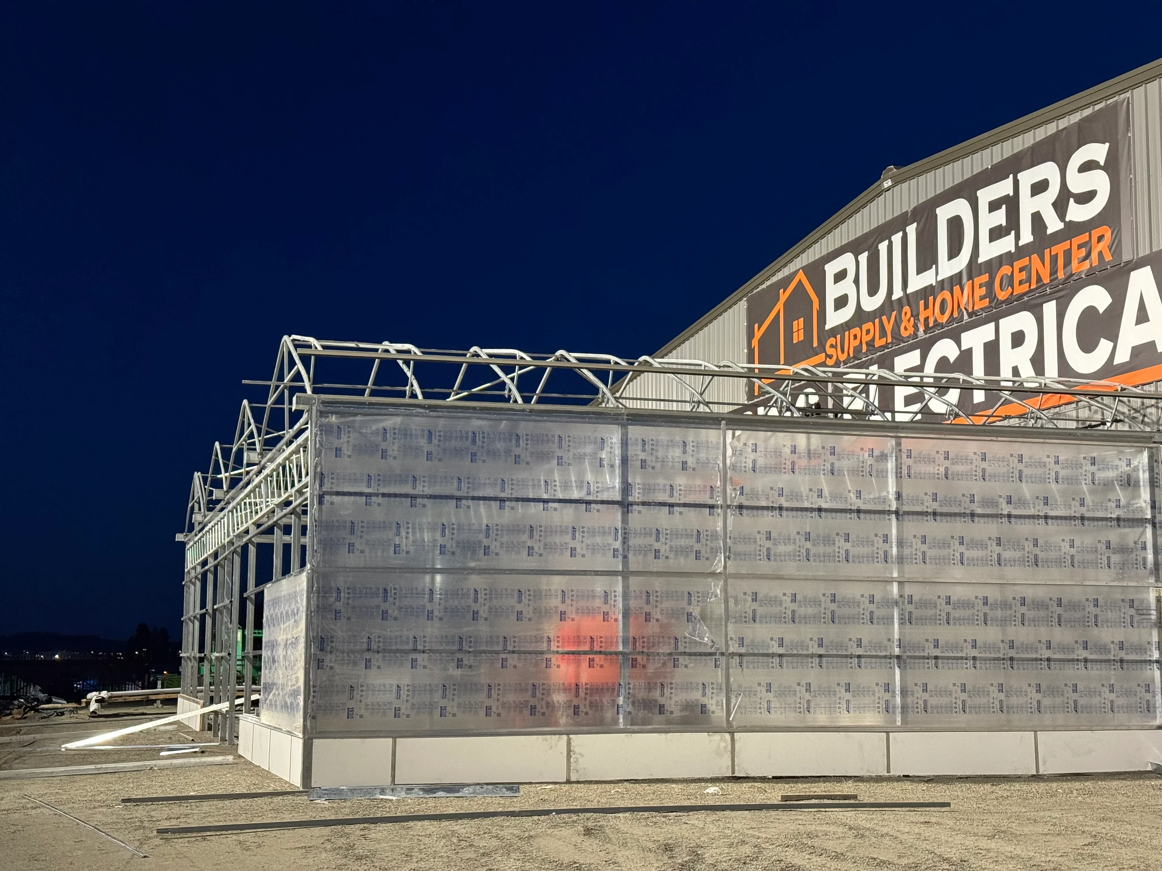 Steel frame commercial building with metal studs, sheathing, and weather barrier under night lighting