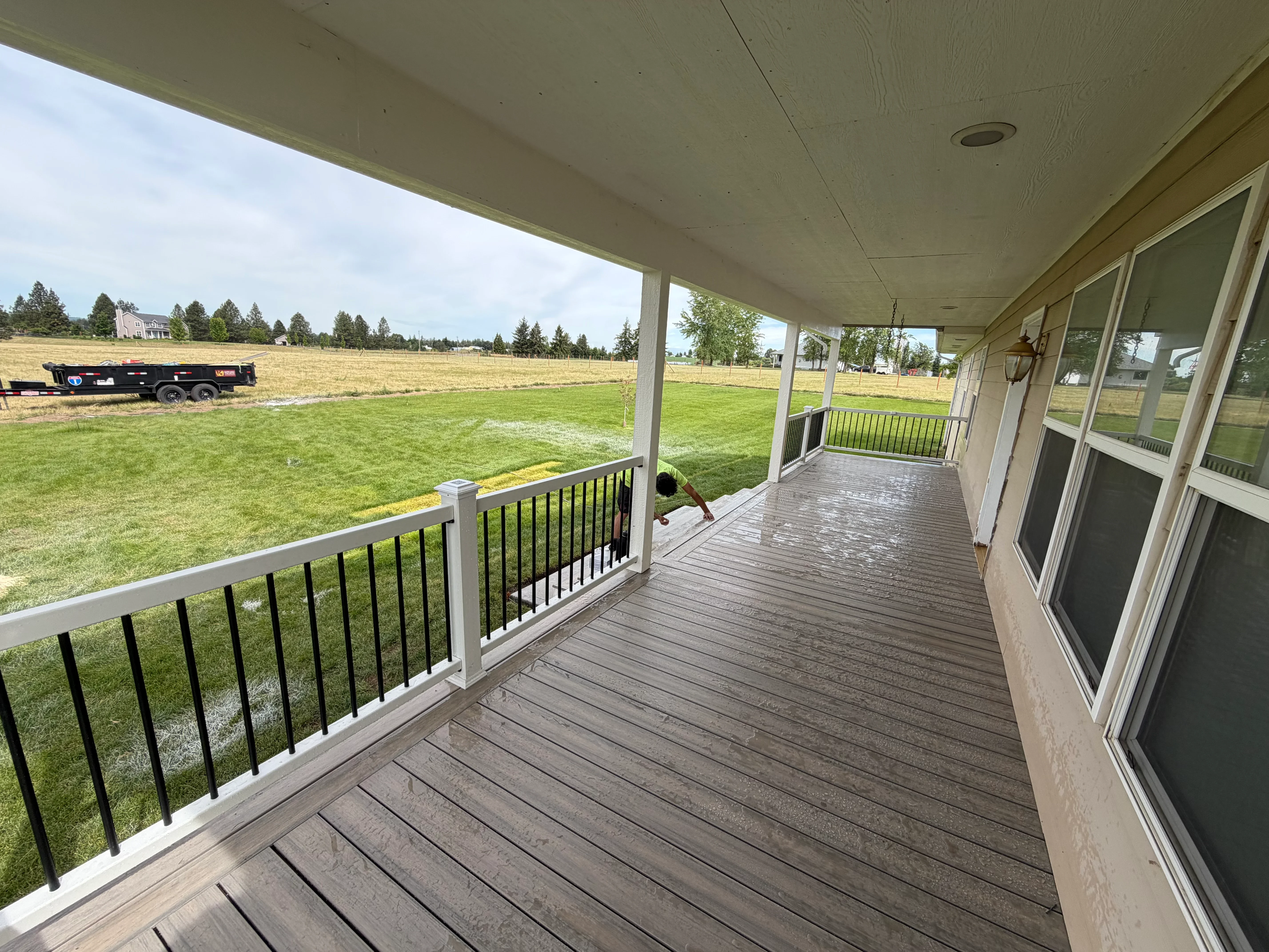 Covered composite deck with white posts, black metal railings, and sliding glass doors overlooking rural property