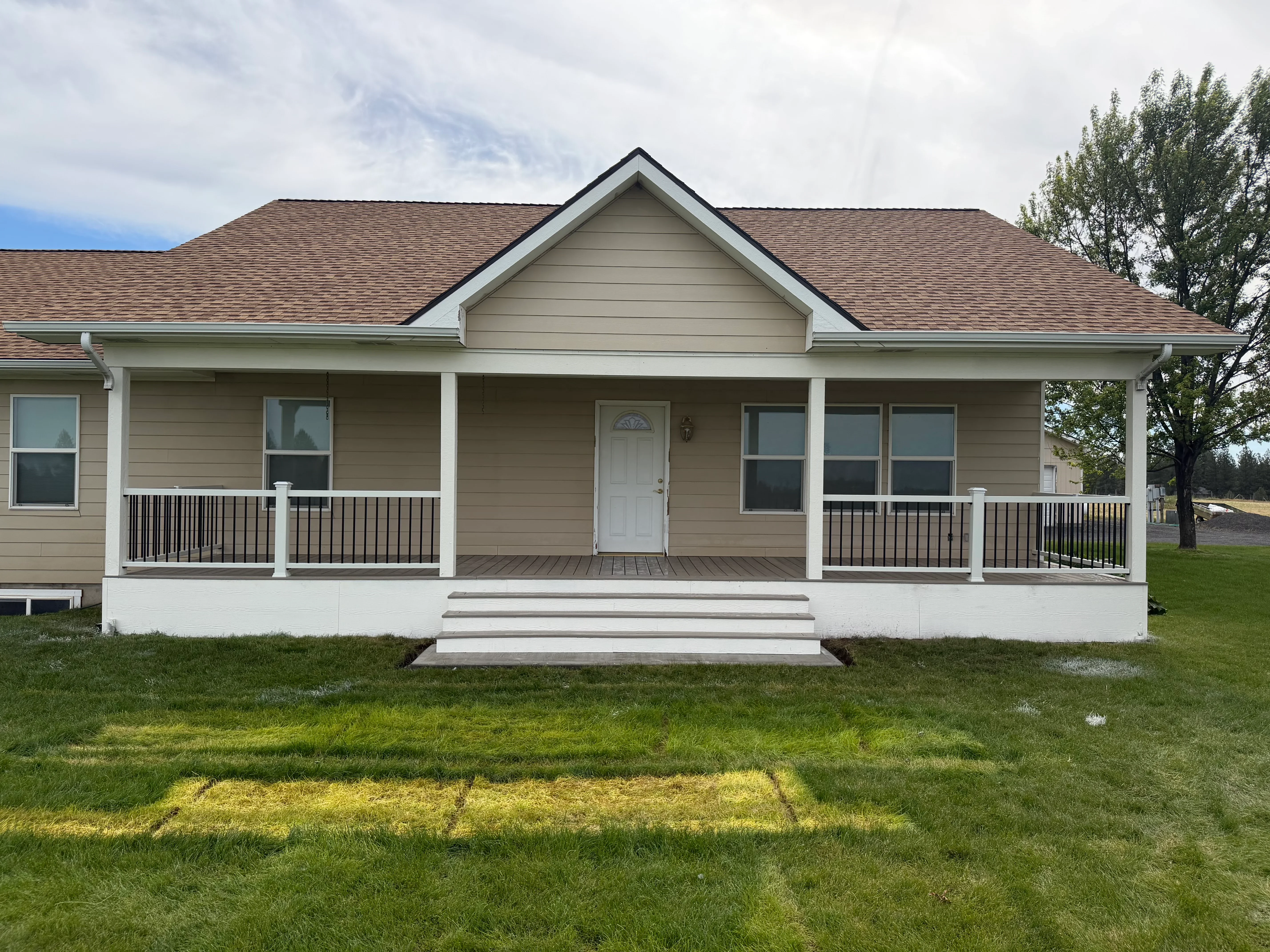 Tan fiber cement siding home with new roof, white porch, black metal railings, and composite deck