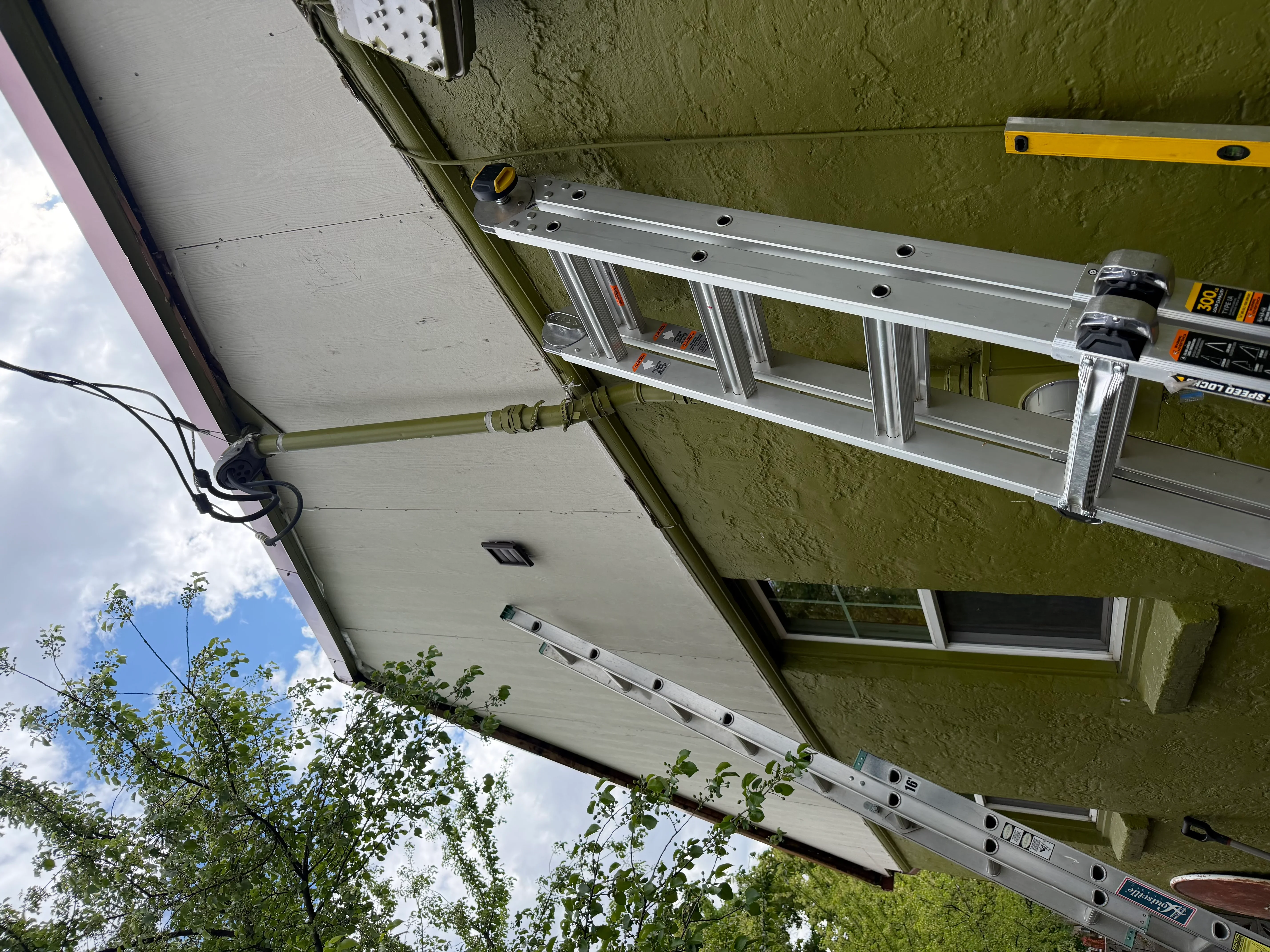 Aluminum soffit trim installation with level and measuring tools against stucco wall