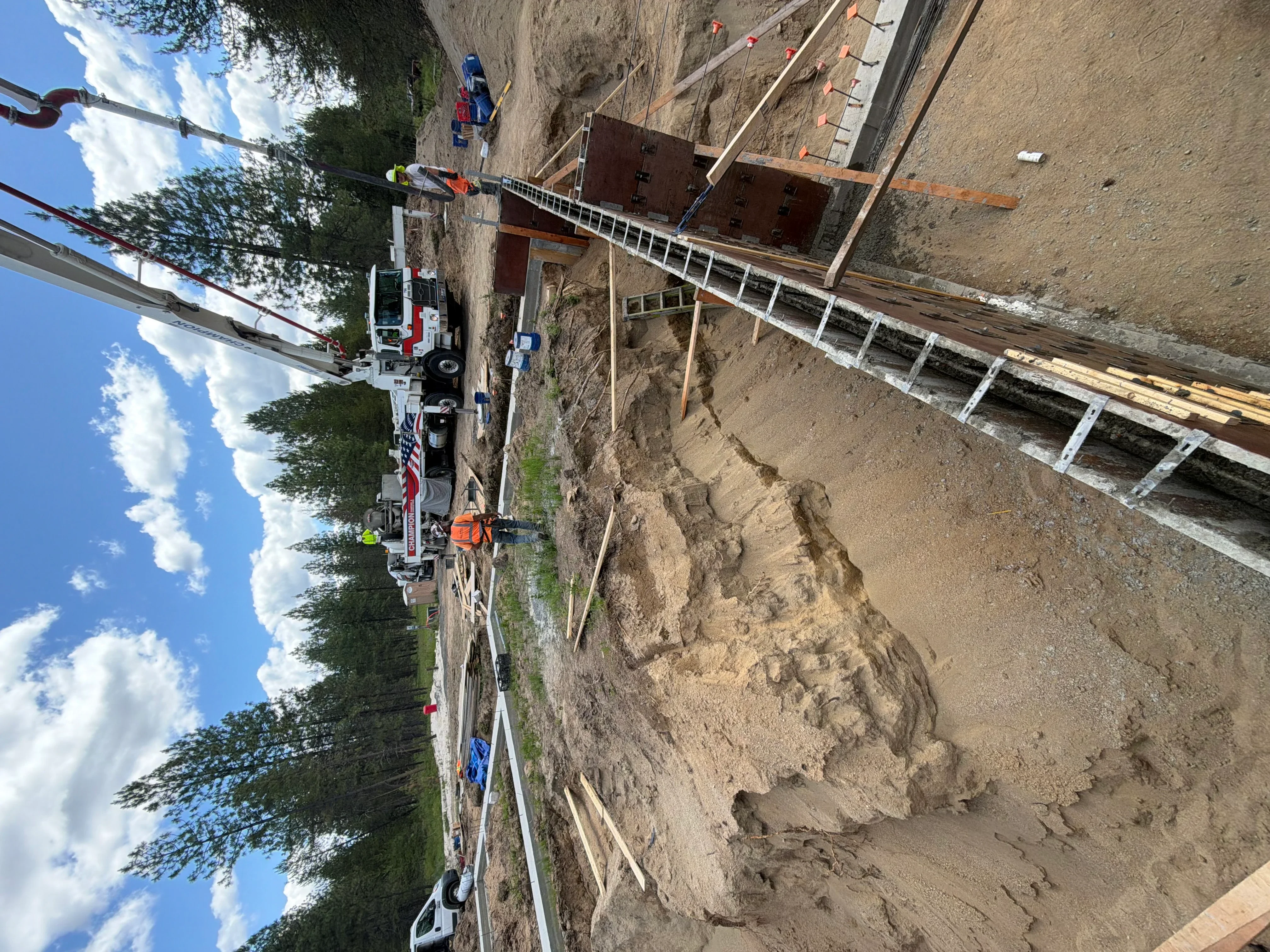 Excavation site with steel shoring, aluminum scaffolding, and heavy equipment during foundation preparation