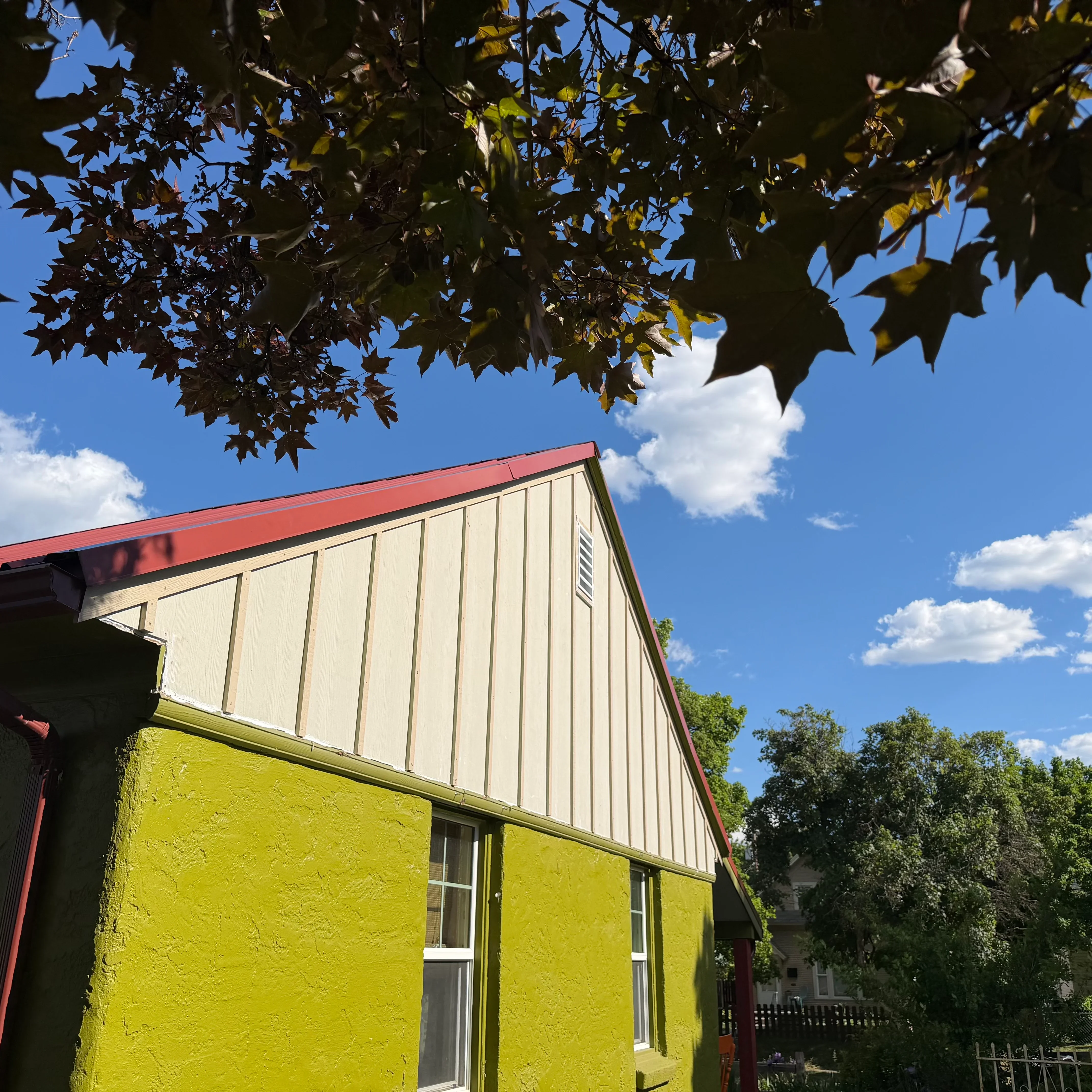 Metal roof with red trim and yellow stucco siding on residential building