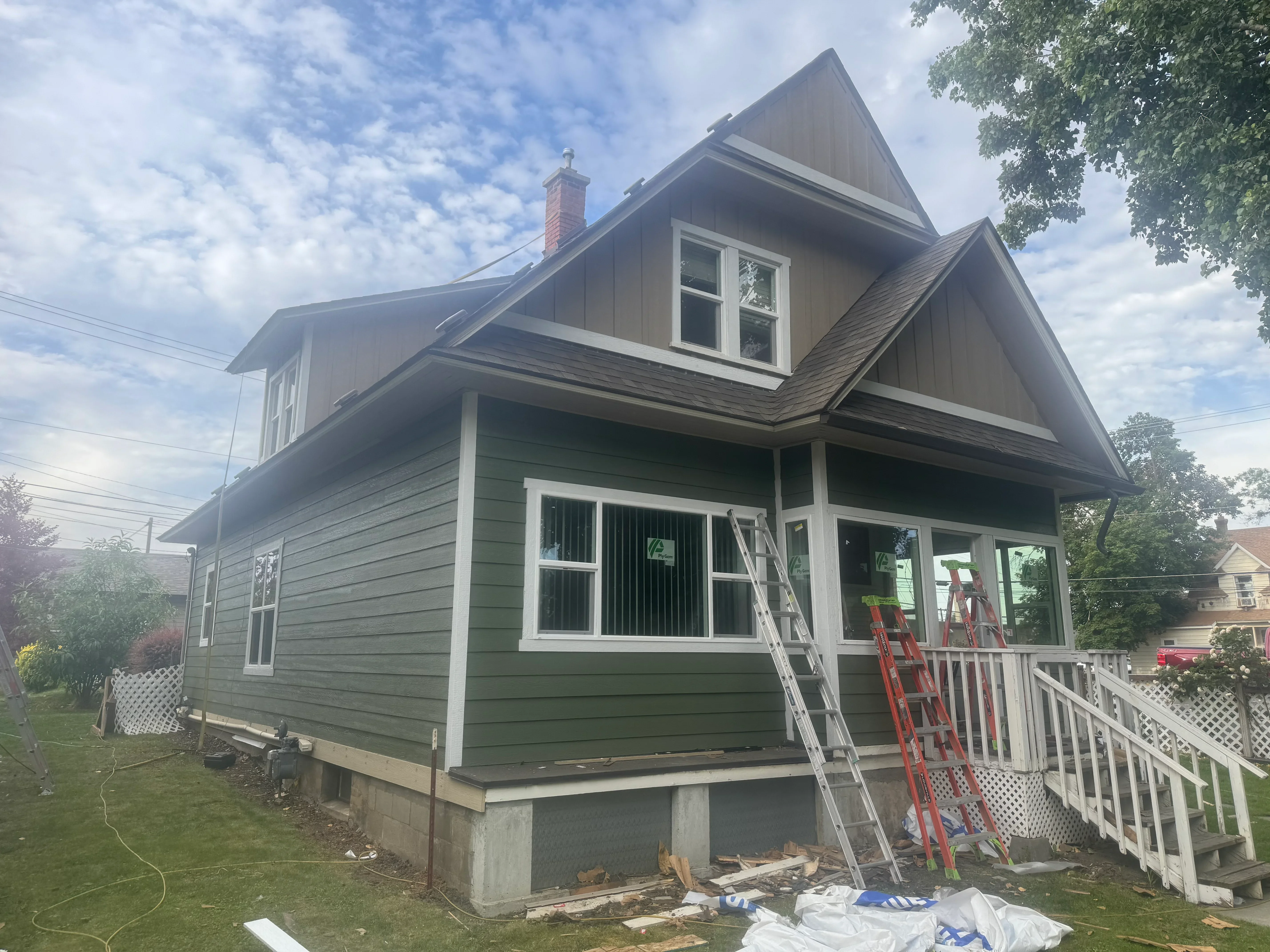 Two-story home with new sage green fiber cement siding, white trim, metal roof, and covered porch during renovation