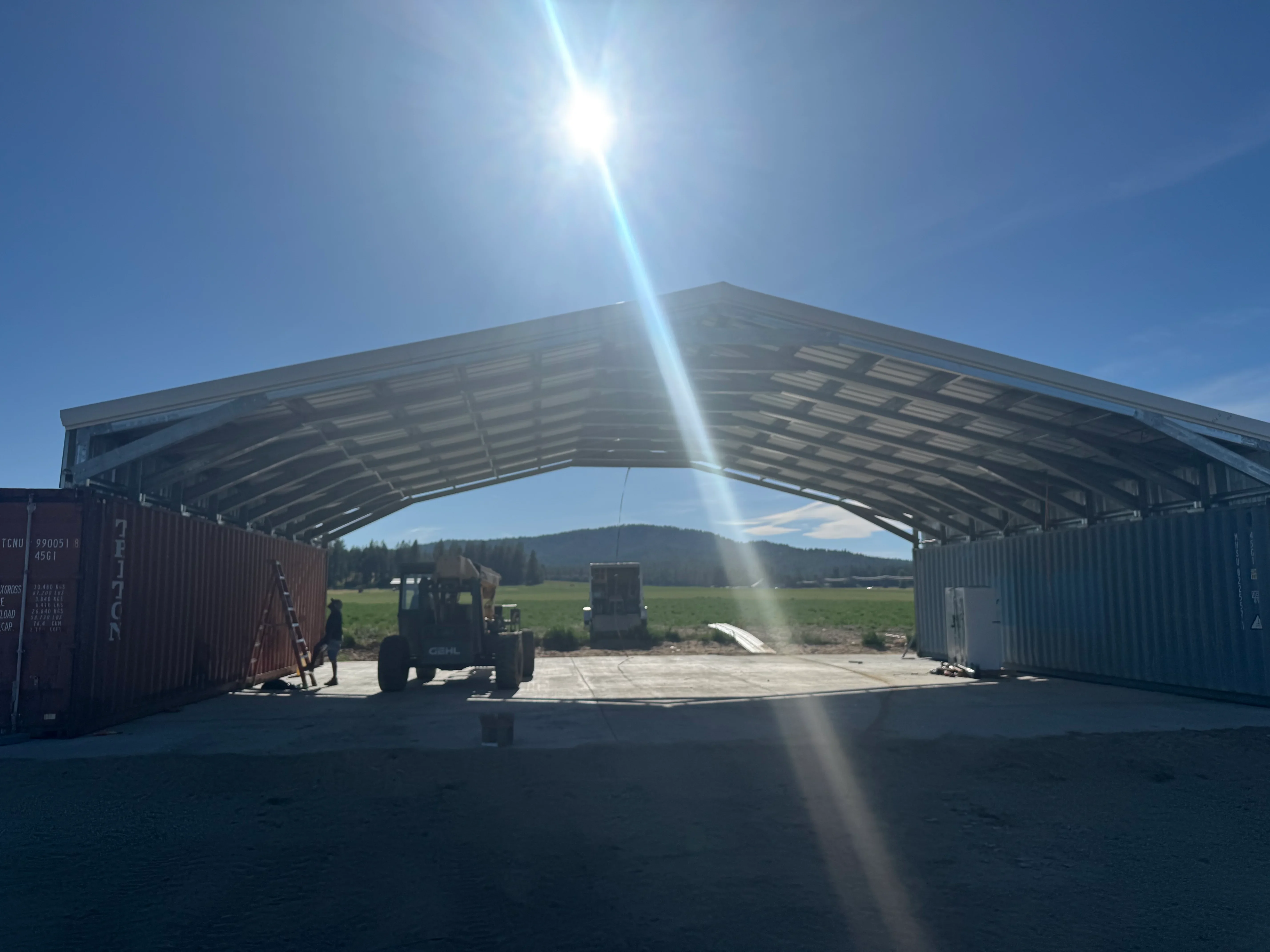 Metal carport with curved steel roof and shipping container walls on concrete pad