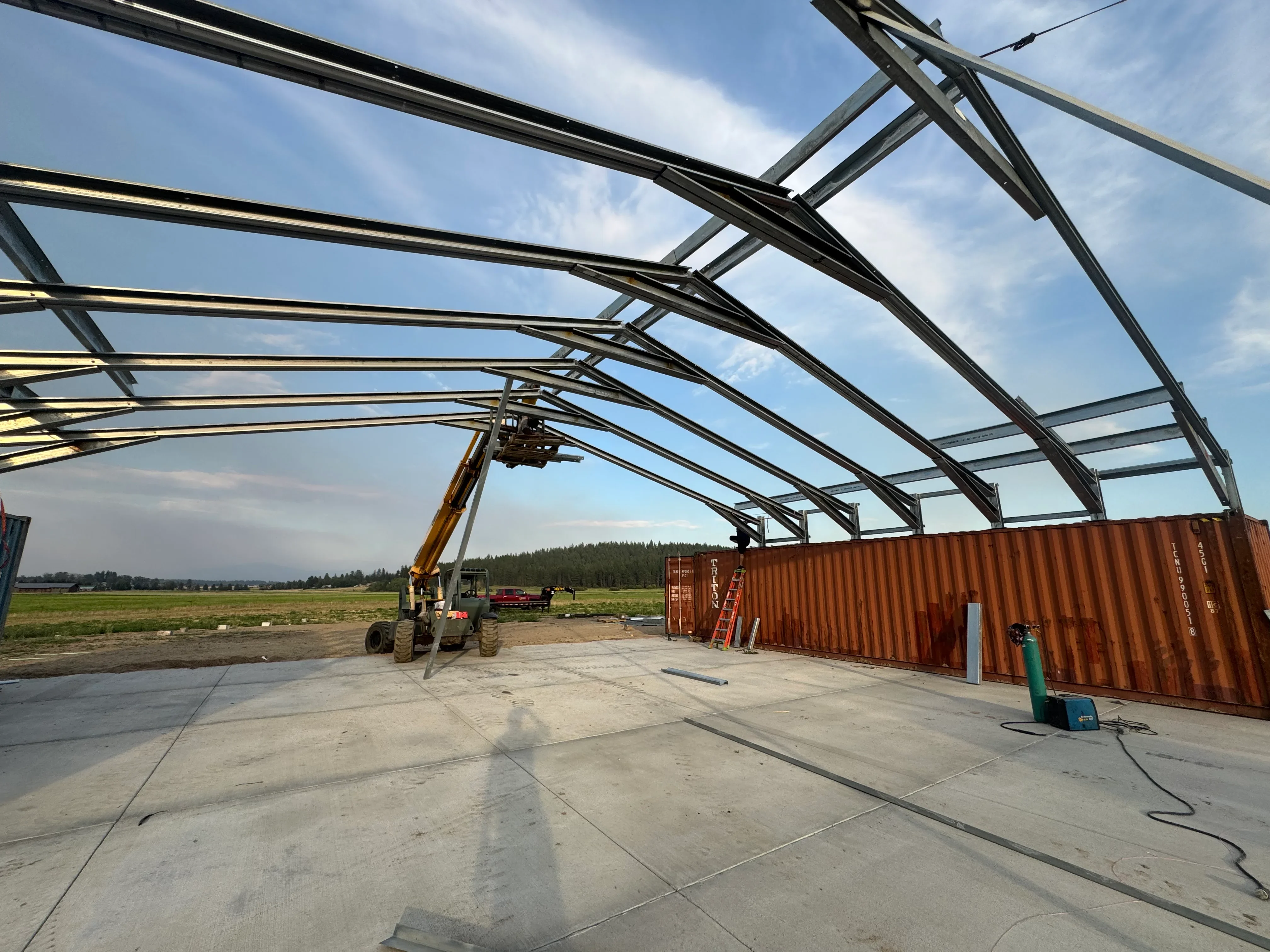 Steel frame agricultural building with welded beams, concrete foundation, and overhead crane system under construction