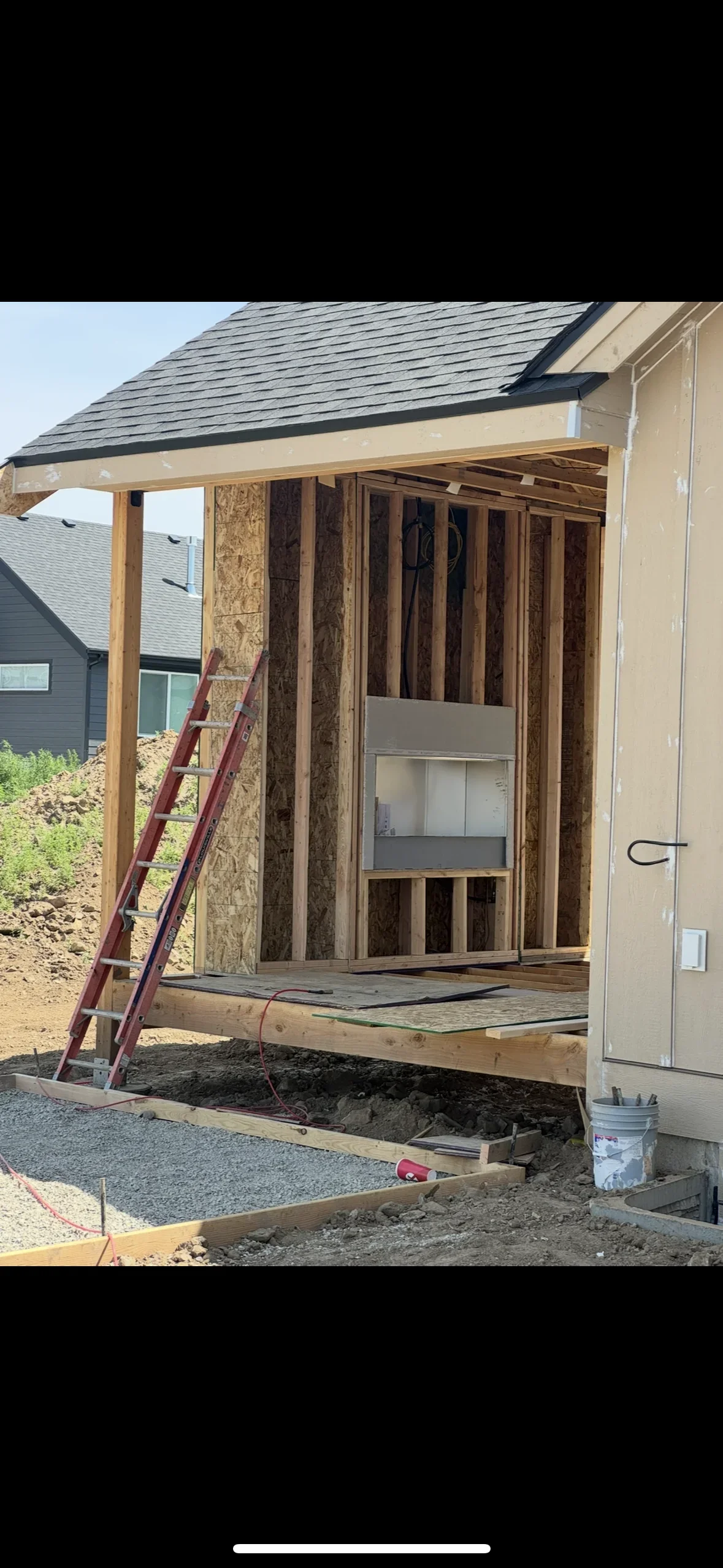 Wood-framed residential addition with OSB sheathing, asphalt shingle roof, and covered porch under construction