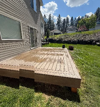 Pressure-treated wood ground level deck with bench seating attached to residential home